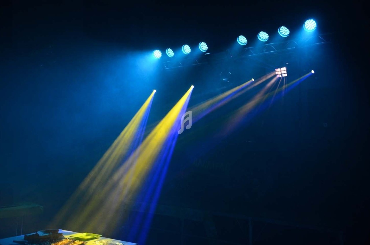 Projecteurs diffusant des faisceaux lumineux jaunes et bleus dans une salle sombre.