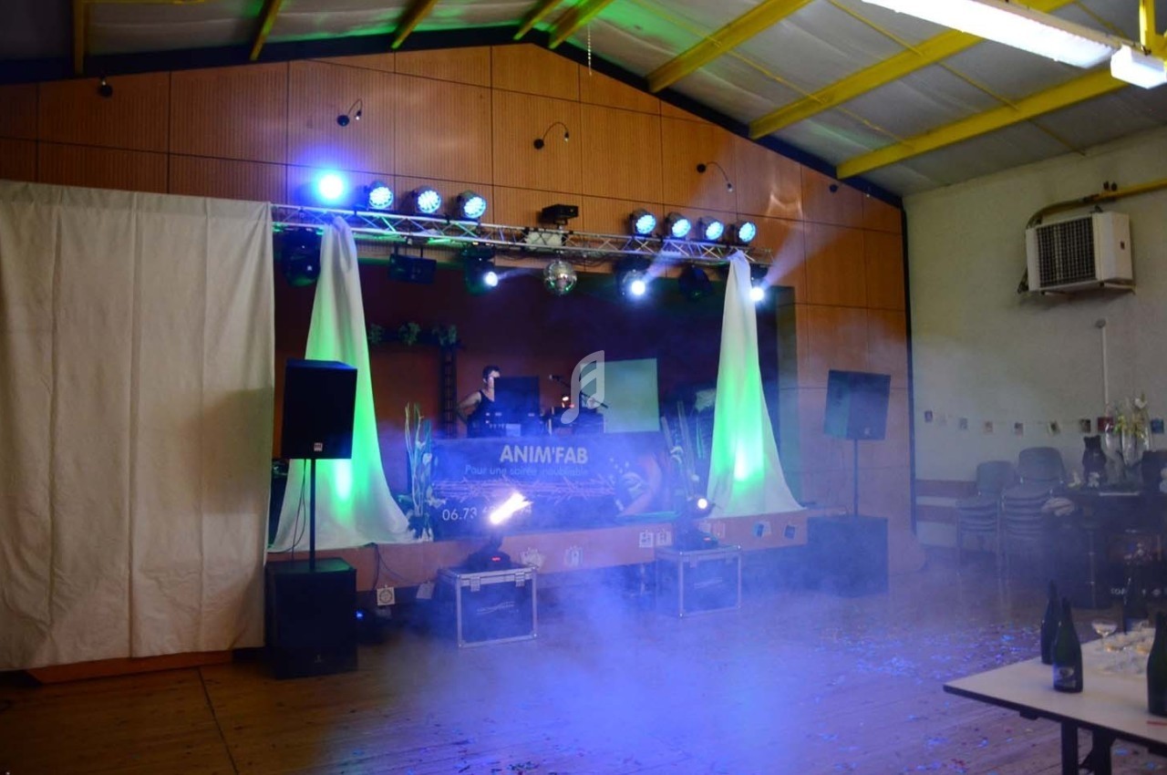 Scène de fête avec éclairage coloré, fumée et équipement de sonorisation dans une salle décorée.