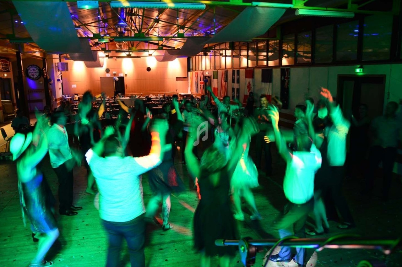 Groupe de personnes dansant sous des lumières colorées dans une salle avec un plafond en structures métalliques.