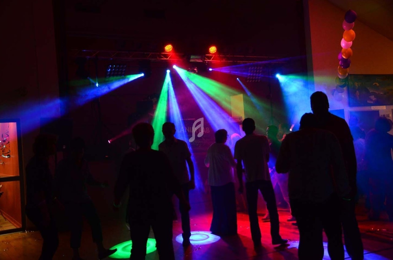 Des personnes dansent dans une salle sombre éclairée par des lumières colorées et des projecteurs.
