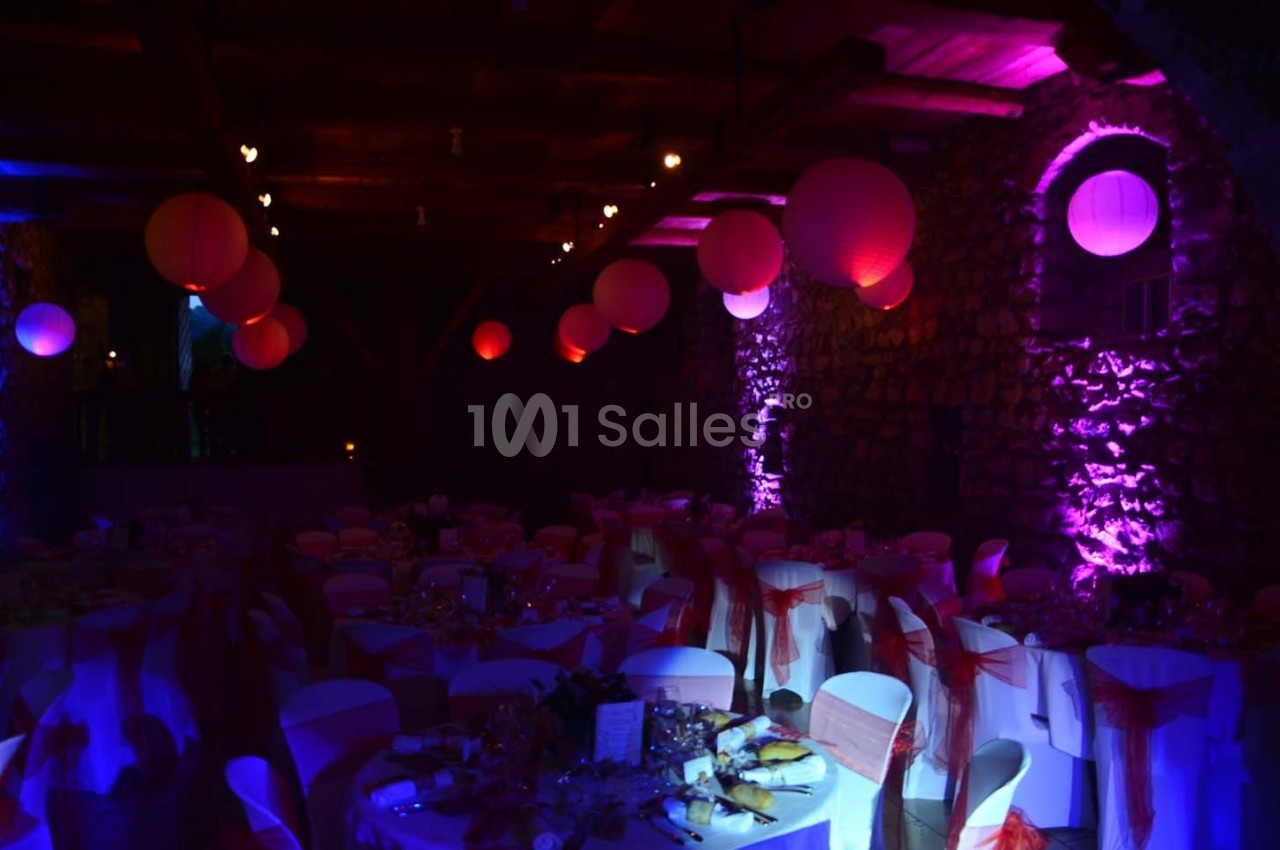 Salle de réception décorée avec des lanternes rouges suspendues, éclairage violet et tables dressées pour un événement.