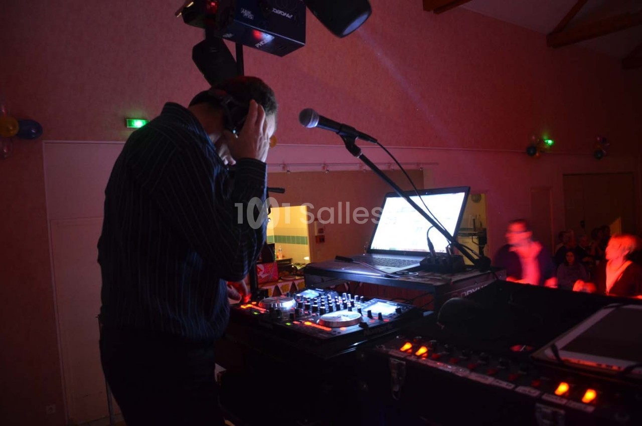 Un DJ mixe de la musique sur une console avec un ordinateur portable dans une salle faiblement éclairée.