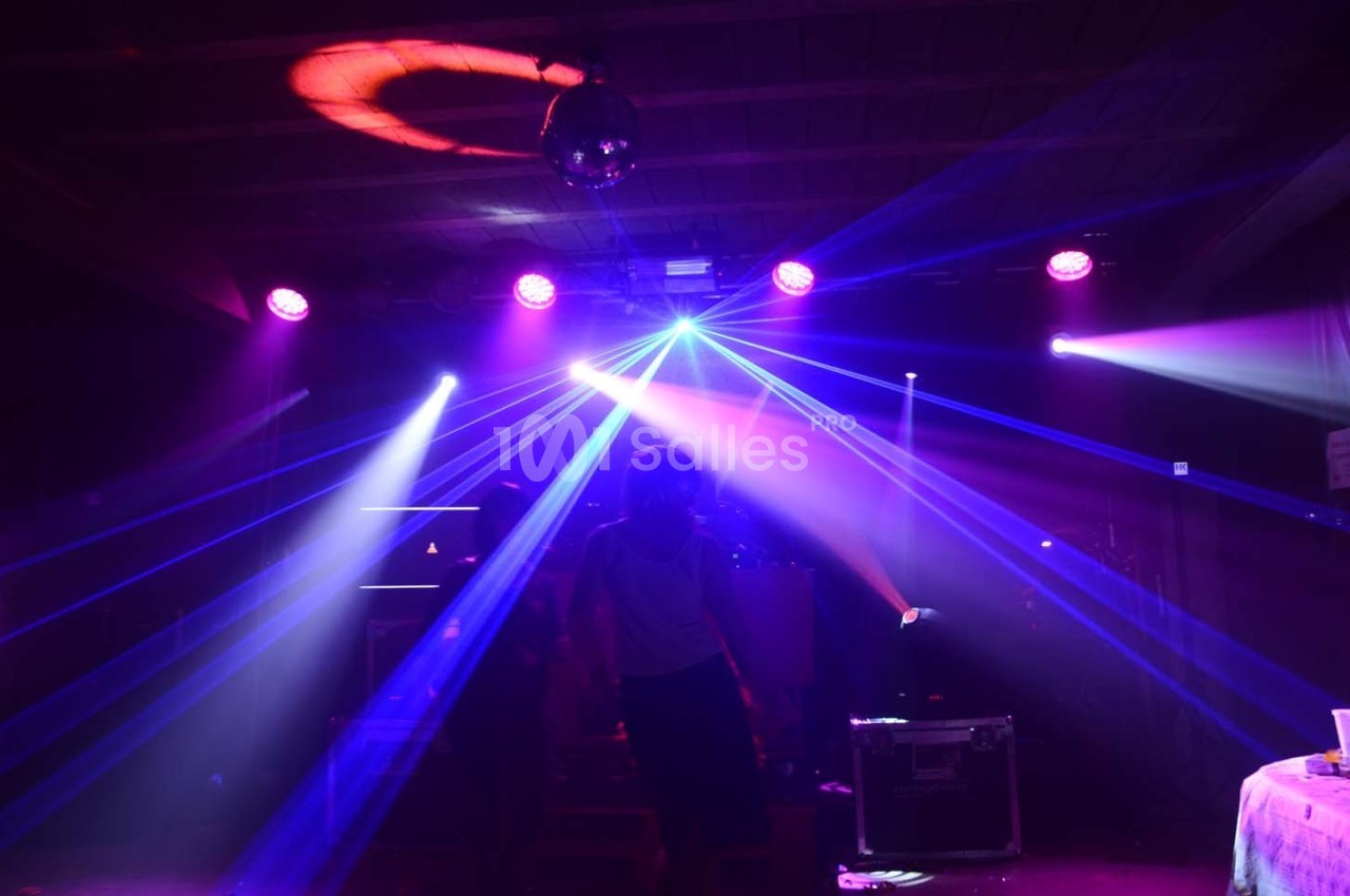 Jeune personne dans une salle sombre éclairée par des faisceaux lumineux colorés et une boule disco au plafond.