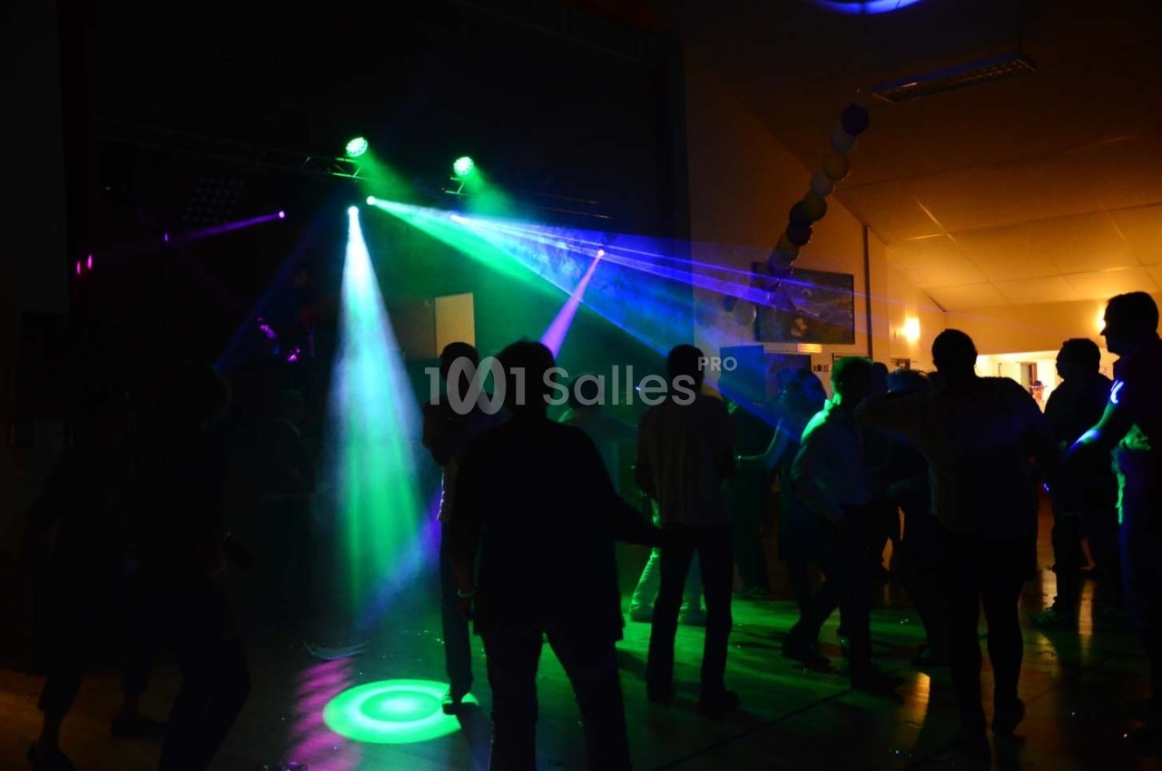 Personnes dansant sous des lumières colorées et des faisceaux laser dans une ambiance festive en intérieur.
