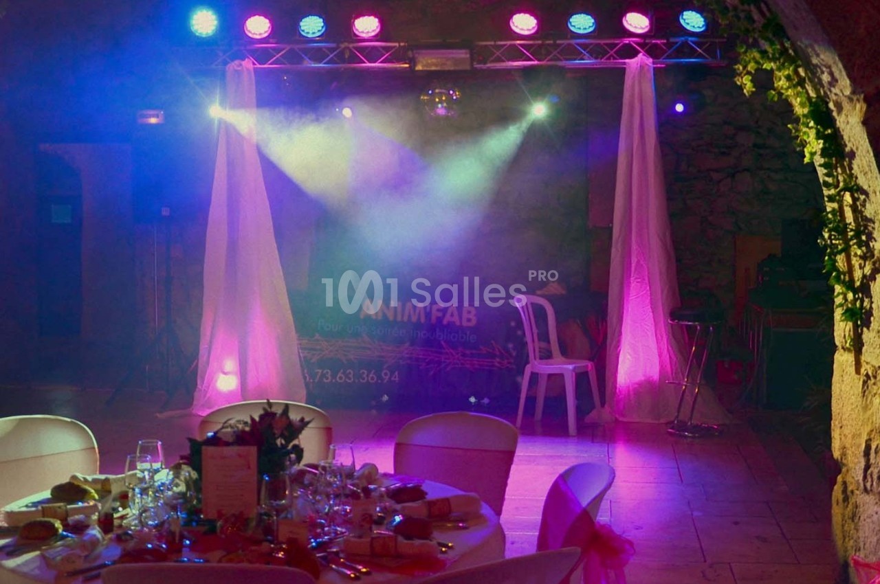 Scène éclairée avec des projecteurs colorés, rideaux blancs et table dressée au premier plan dans une salle de réception.