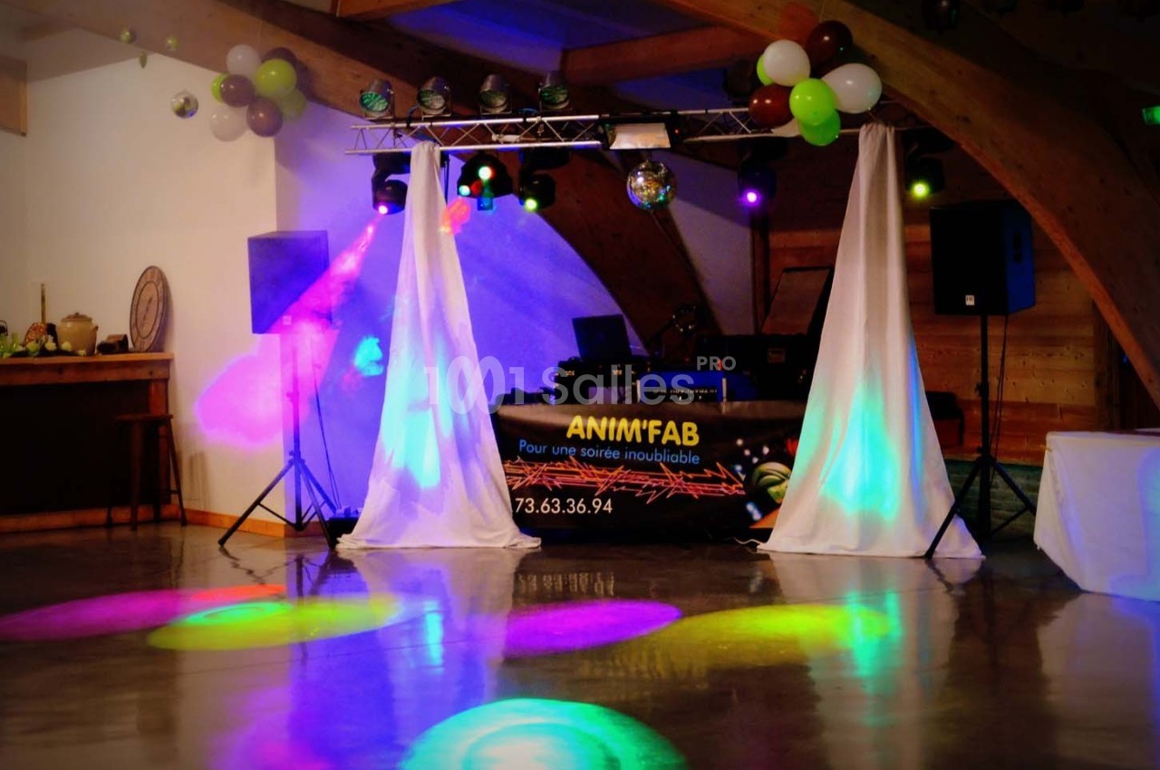 Salle de réception avec piste de danse éclairée par des lumières colorées et un stand de DJ en arrière-plan.