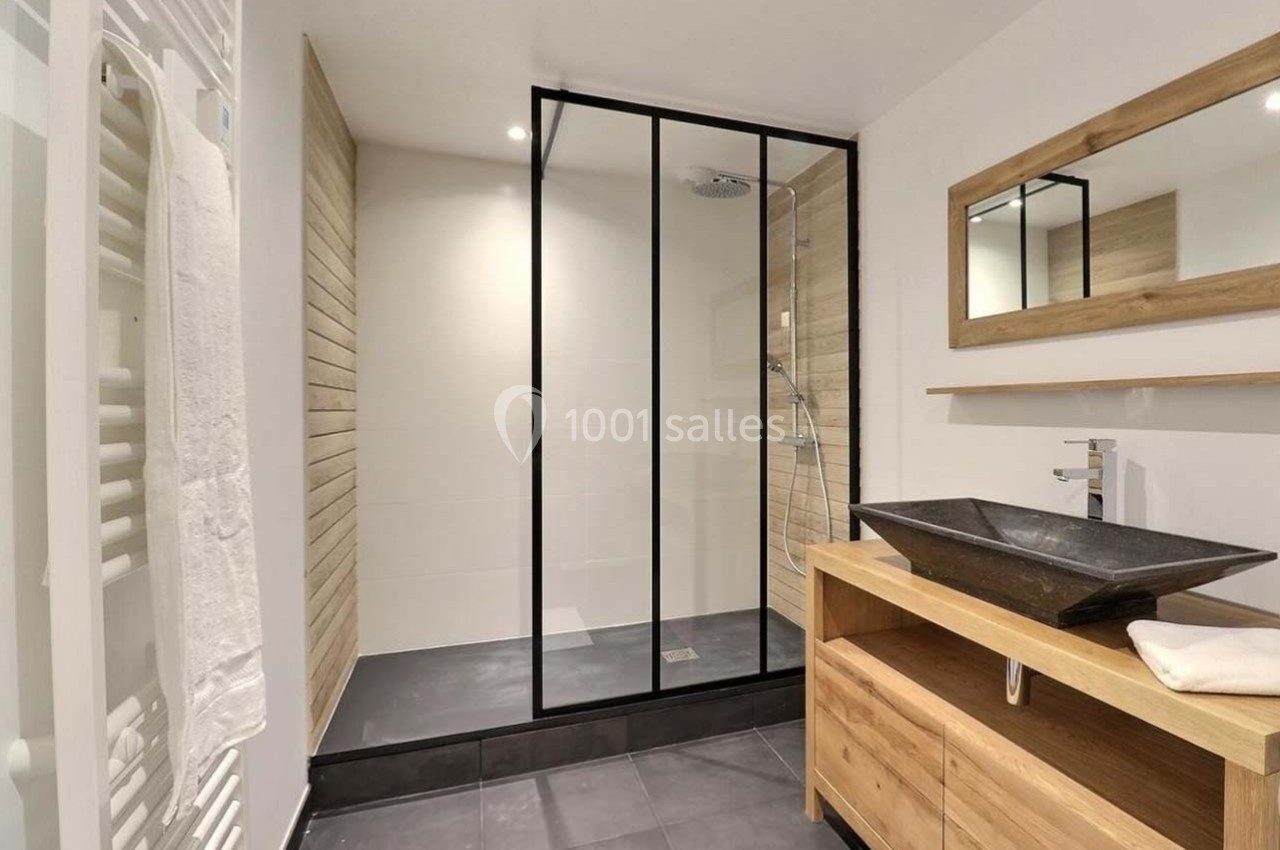 Salle de bain moderne avec douche à l'italienne, meuble en bois avec vasque noire et miroir rectangulaire.