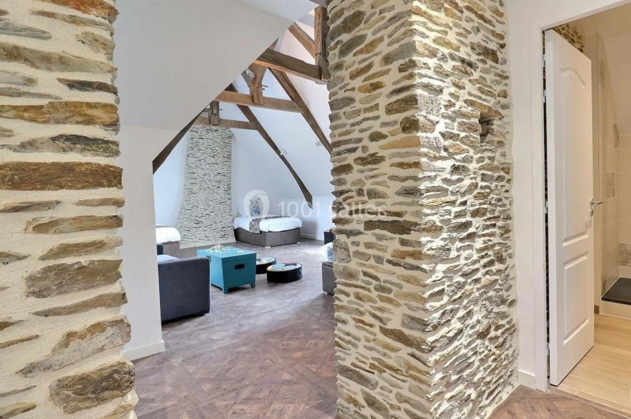 Intérieur lumineux avec murs en pierre apparente, poutres en bois et parquet, menant à une pièce aménagée.
