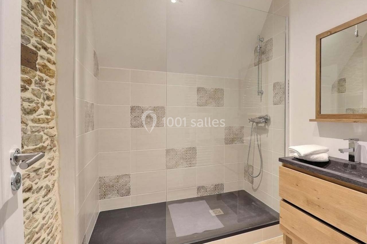Douche à l'italienne avec paroi vitrée, carrelage beige et motifs, meuble en bois clair et miroir au mur.