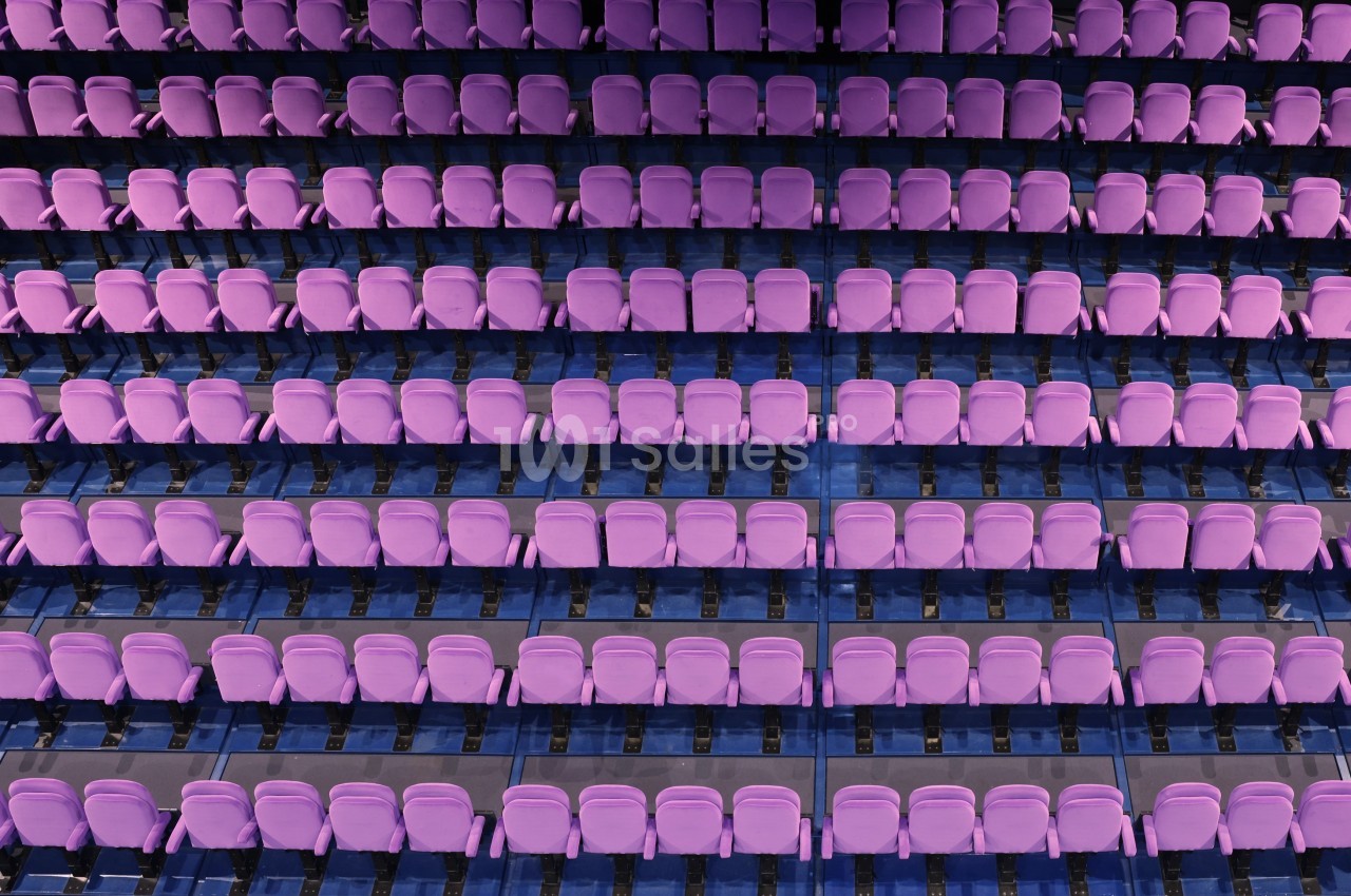 Rangées de sièges violets alignés dans un auditorium vide, vue en plongée.