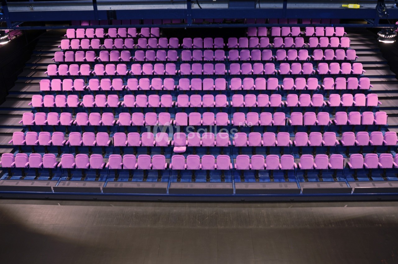 Gradins vides avec des sièges roses alignés dans une salle de spectacle moderne.
