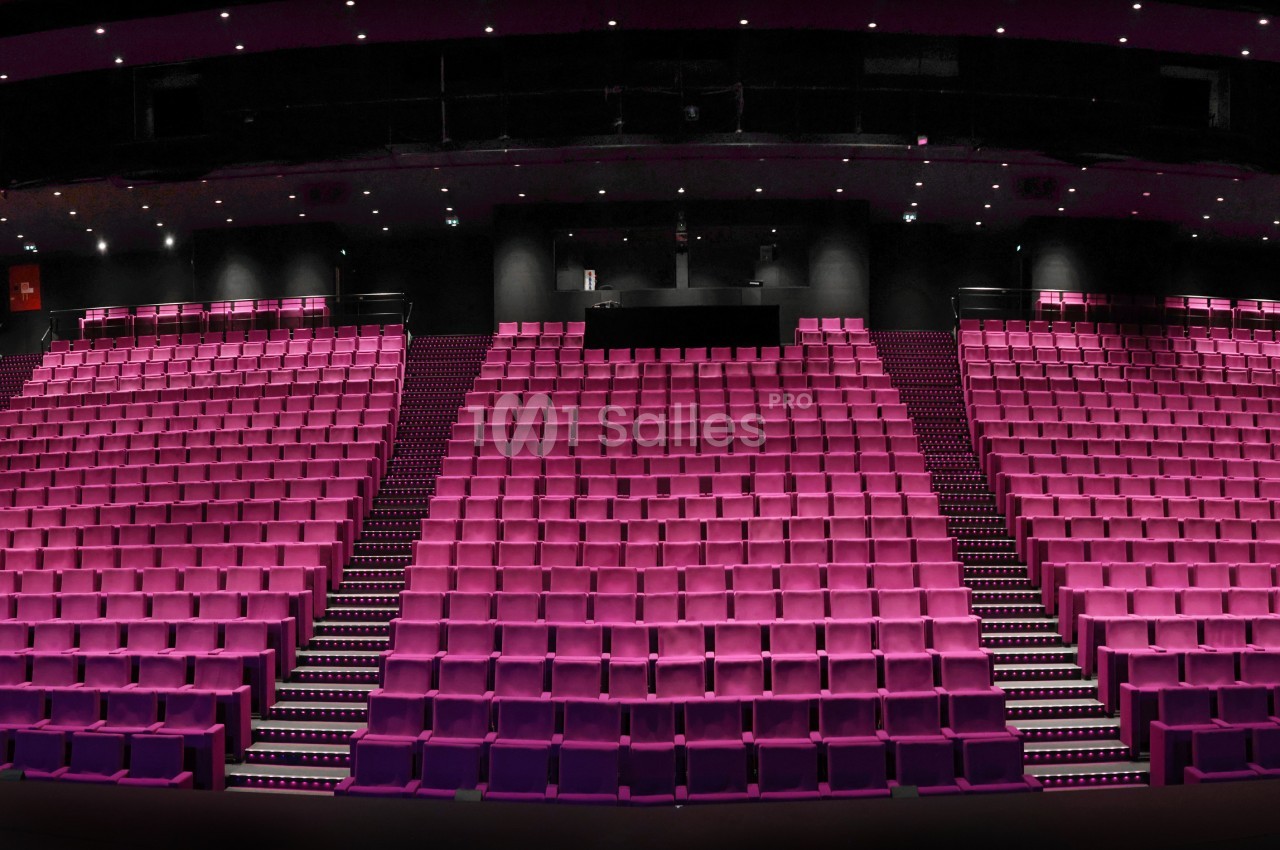 Salle de cinéma avec sièges fuchsia en gradins face à l'écran, éclairage encastré au plafond.