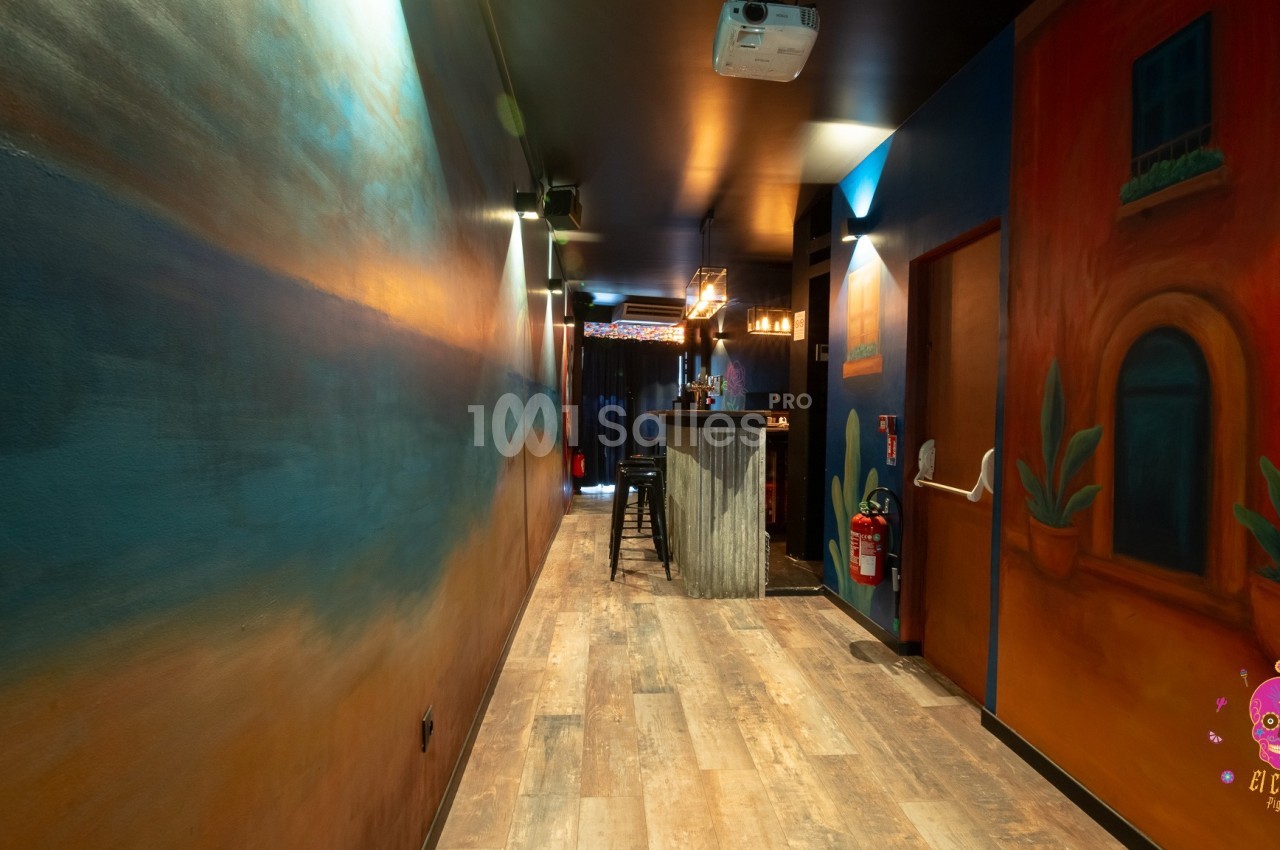 Couloir coloré avec des peintures murales vives menant à un bar éclairé, décoré dans un style chaleureux et accueillant.