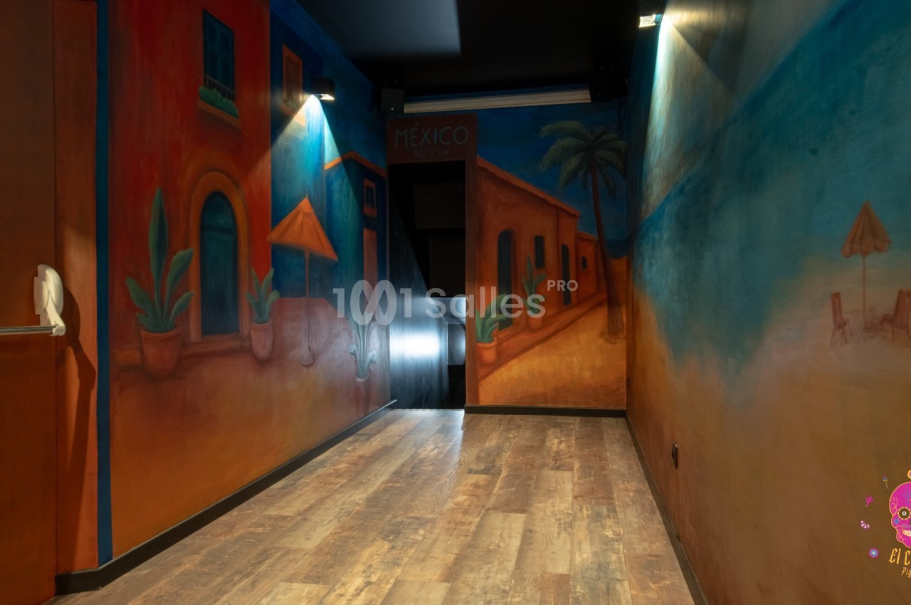 Mur peint représentant un paysage mexicain avec maisons colorées, palmiers et plage, dans une pièce au sol en bois.