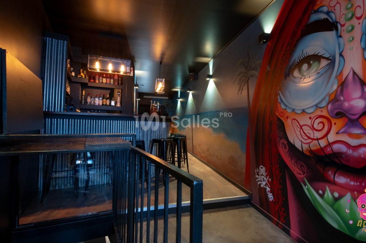 Intérieur d'un bar avec un mur décoré d'une fresque colorée représentant un visage, éclairage tamisé.