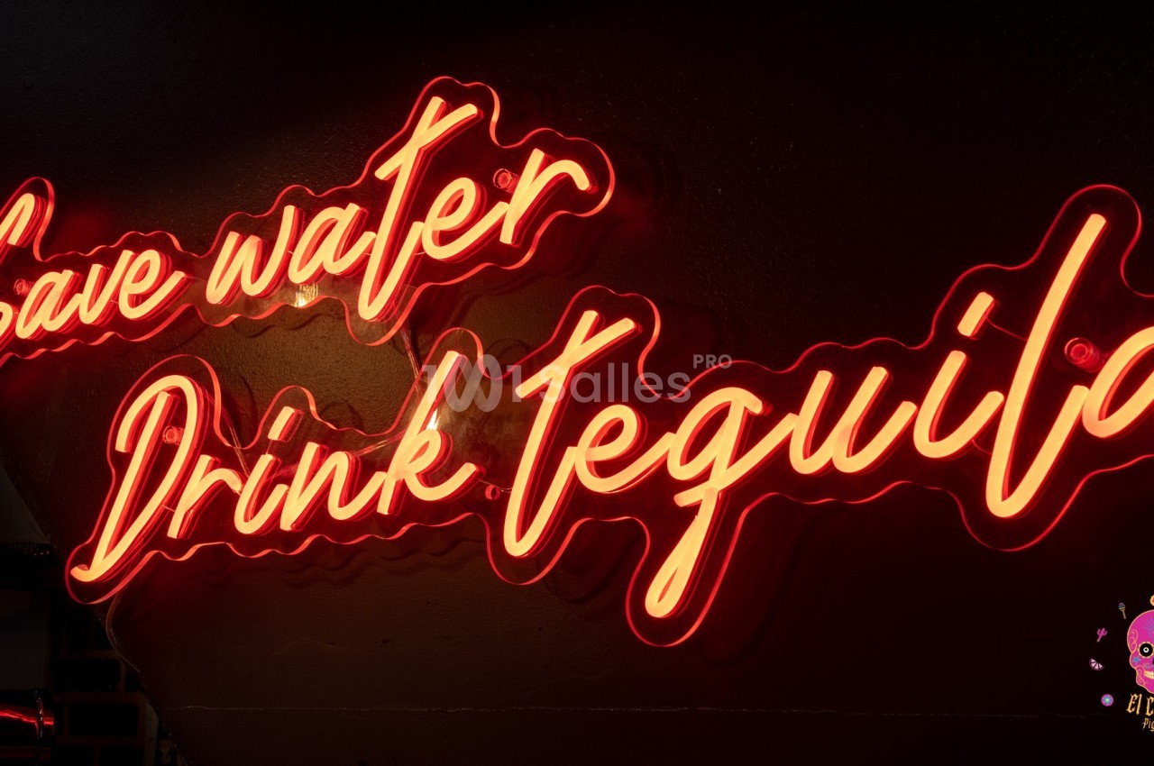 Enseigne néon rouge avec l'inscription ’Save water, Drink tequila’ sur un mur sombre.