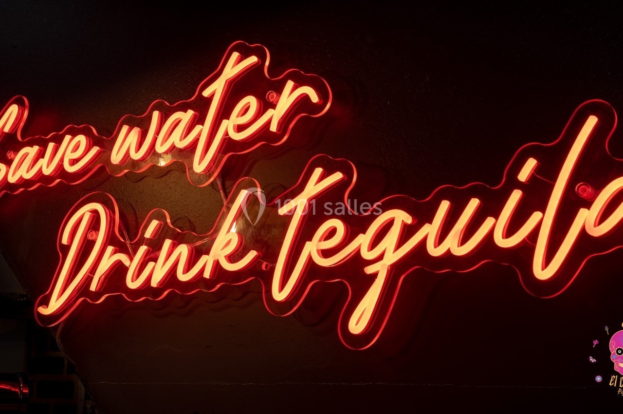 Texte néon rouge indiquant ’Save water, Drink tequila’ sur un mur sombre.