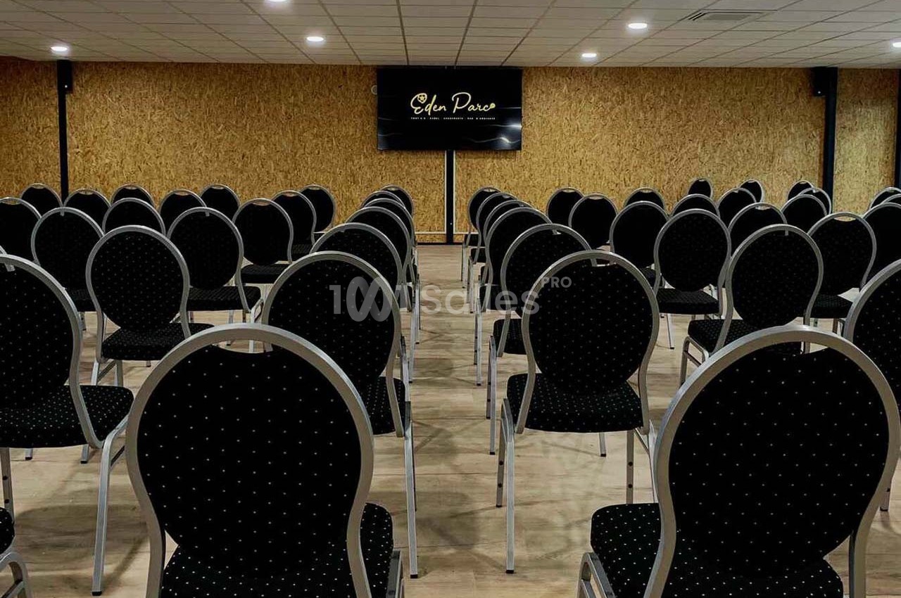 Salle de conférence avec des rangées de chaises noires alignées face à un écran mural allumé.
