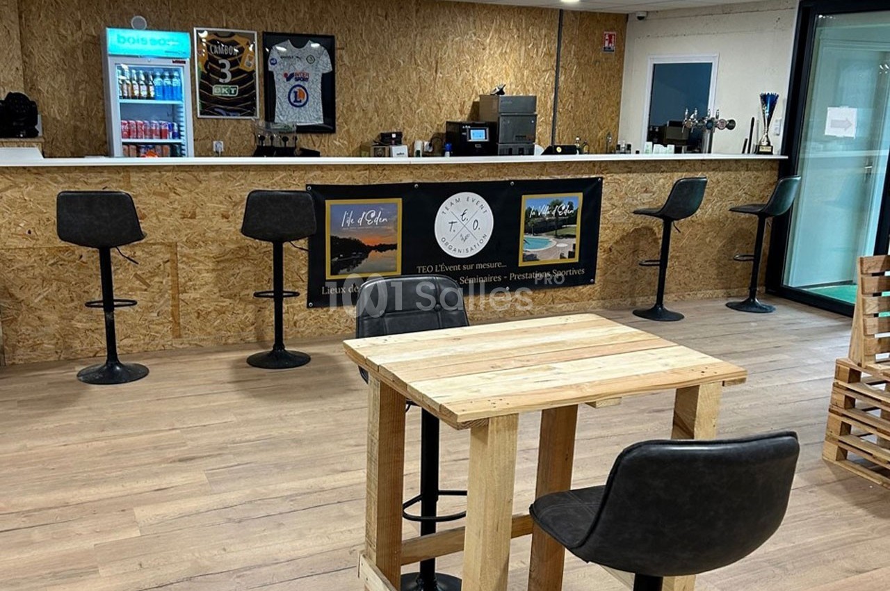 Un espace intérieur avec un comptoir en bois, des tabourets hauts, une table en bois et un sol en parquet clair.