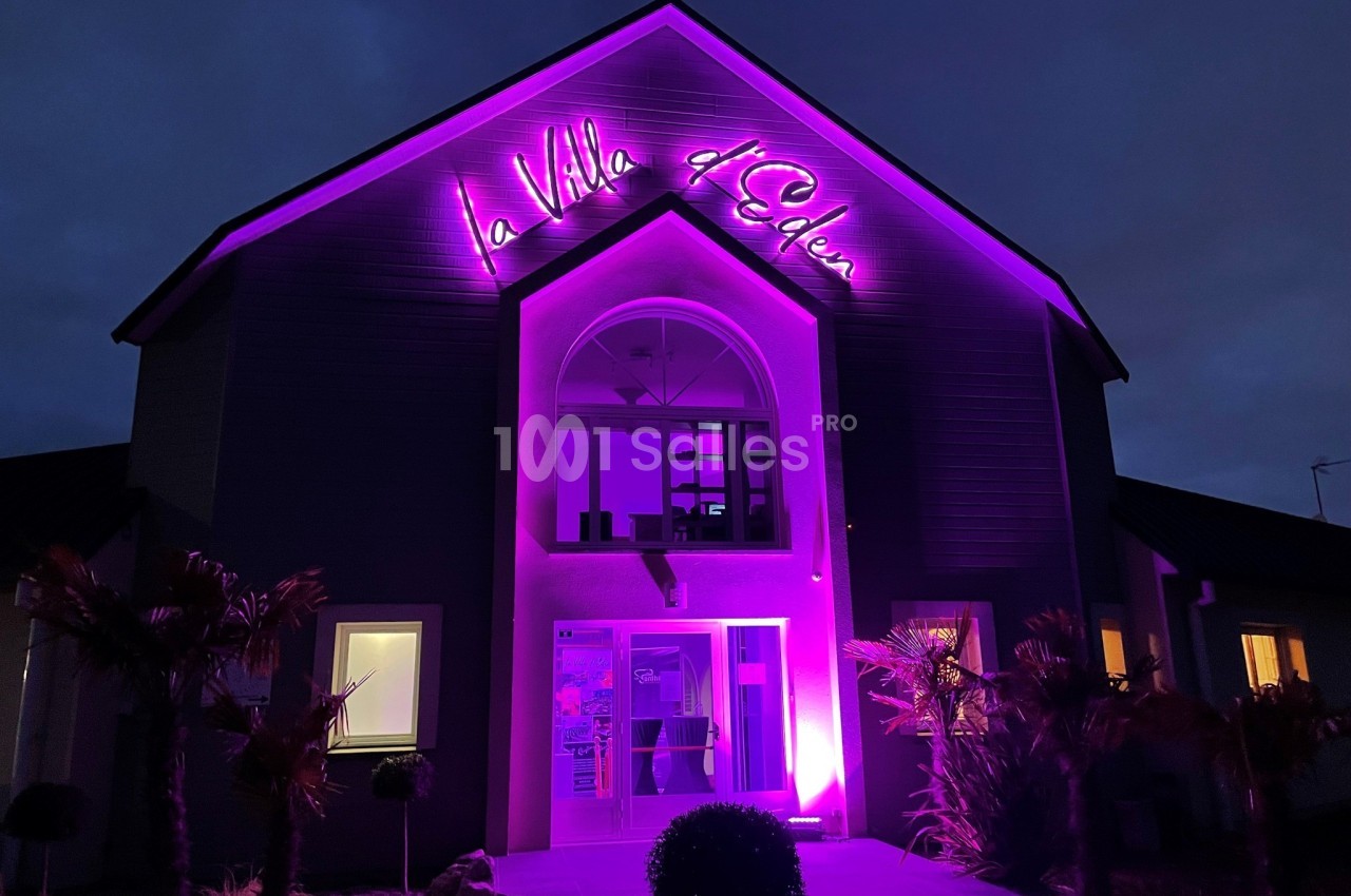Façade d'un bâtiment éclairé en violet avec une enseigne lumineuse indiquant ’La Villa d'Eden’ de nuit.