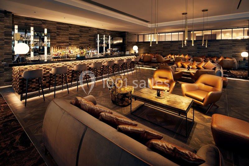 Bar moderne avec comptoir éclairé, tabourets hauts, fauteuils en cuir et éclairage tamisé dans une ambiance chaleureuse.