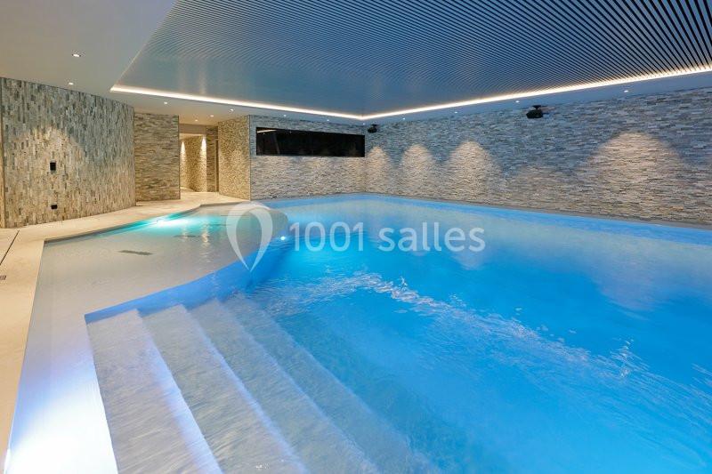 Piscine intérieure moderne avec éclairage tamisé, murs en pierre et plafond à lames.