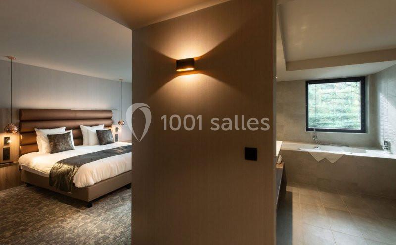 Chambre d'hôtel moderne avec lit double, éclairage tamisé, et salle de bain attenante avec baignoire près d'une fenêtre.