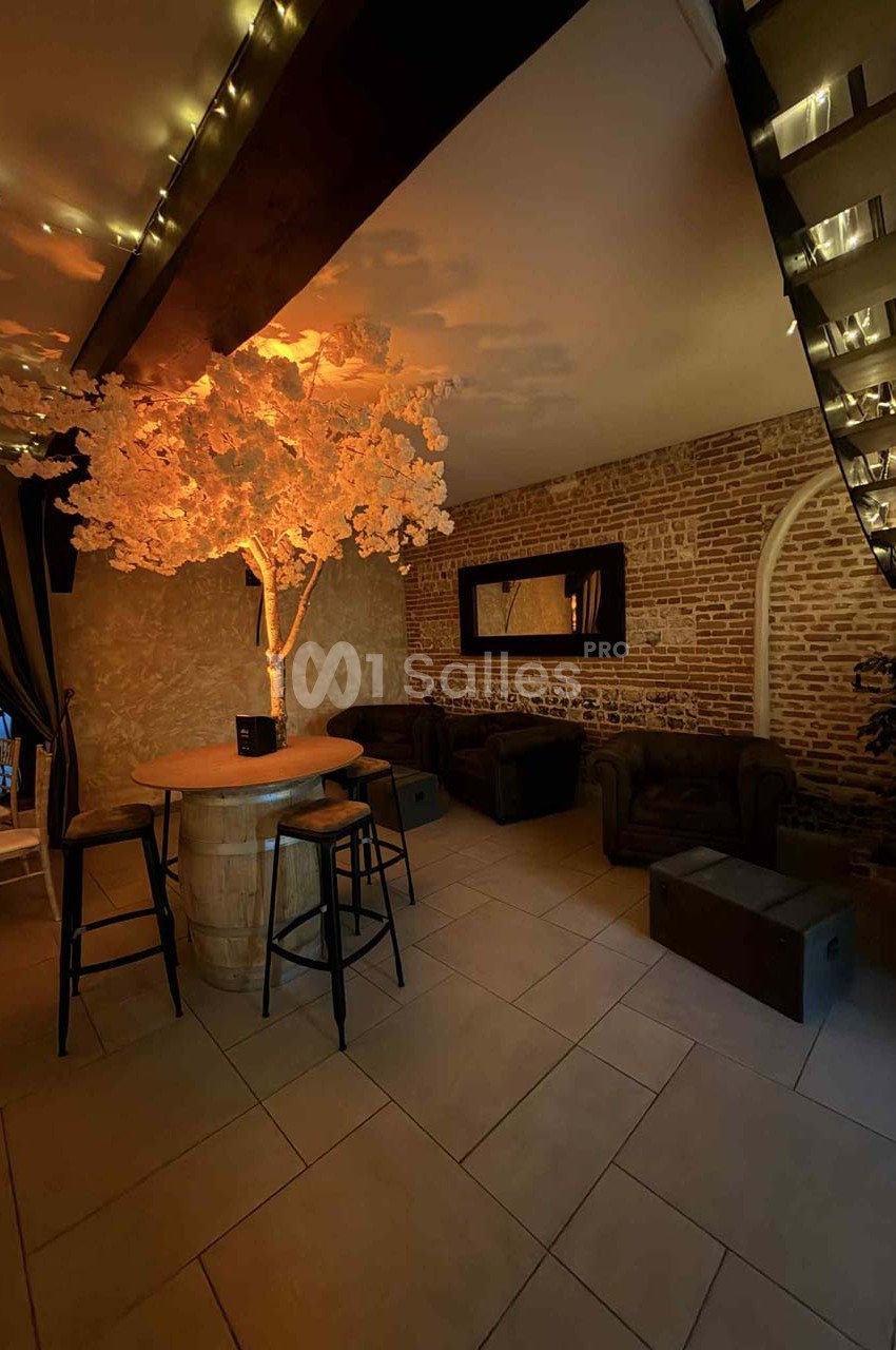 Espace intérieur avec un arbre lumineux décoratif, des fauteuils en cuir, un mur en briques et un bar en tonneau.