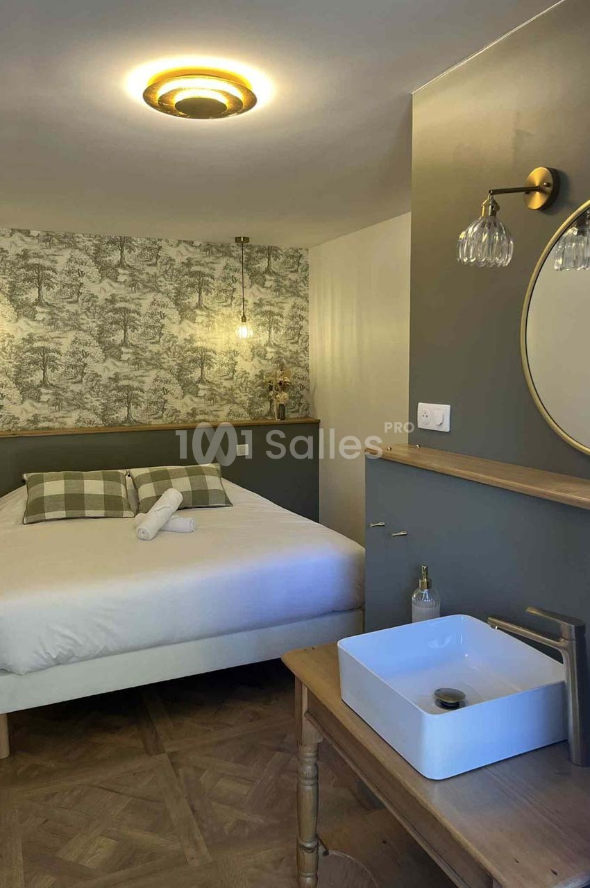 Chambre avec lit double, mur décoré de papier peint, lavabo sur meuble en bois et éclairage chaleureux.