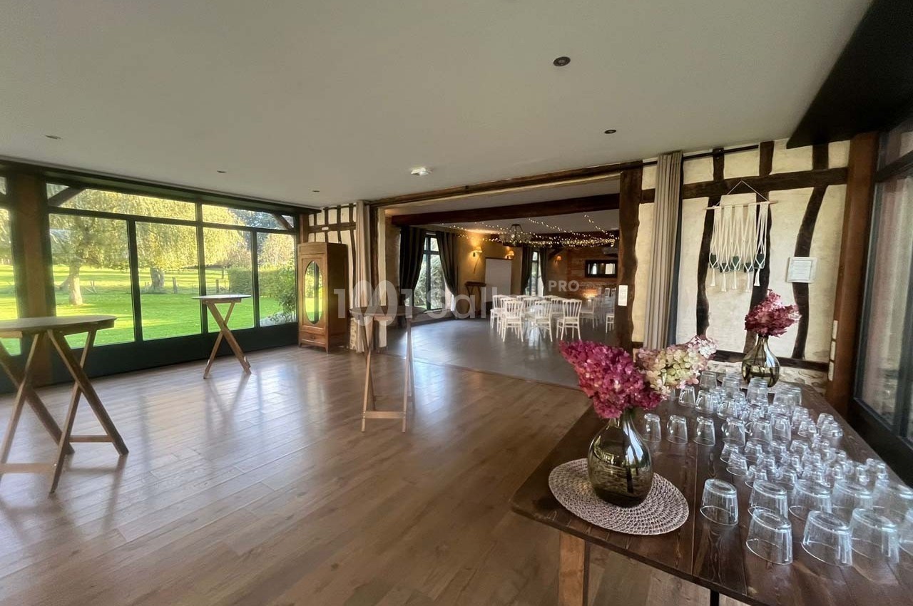 Salle lumineuse avec parquet, tables en bois, décorations florales et baies vitrées donnant sur un espace extérieur…