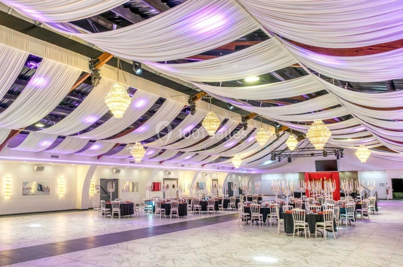 Salle de réception élégante avec tables dressées, lustres suspendus et plafond décoré de drapés blancs.