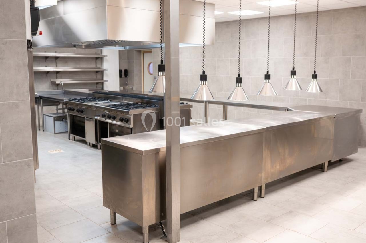 Cuisine professionnelle moderne avec équipements en acier inoxydable, plan de travail et luminaires suspendus.