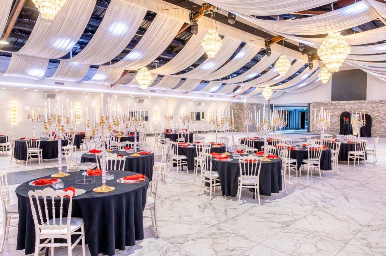 Salle de réception élégante avec tables rondes dressées, nappes noires, décorations dorées et lustres suspendus.