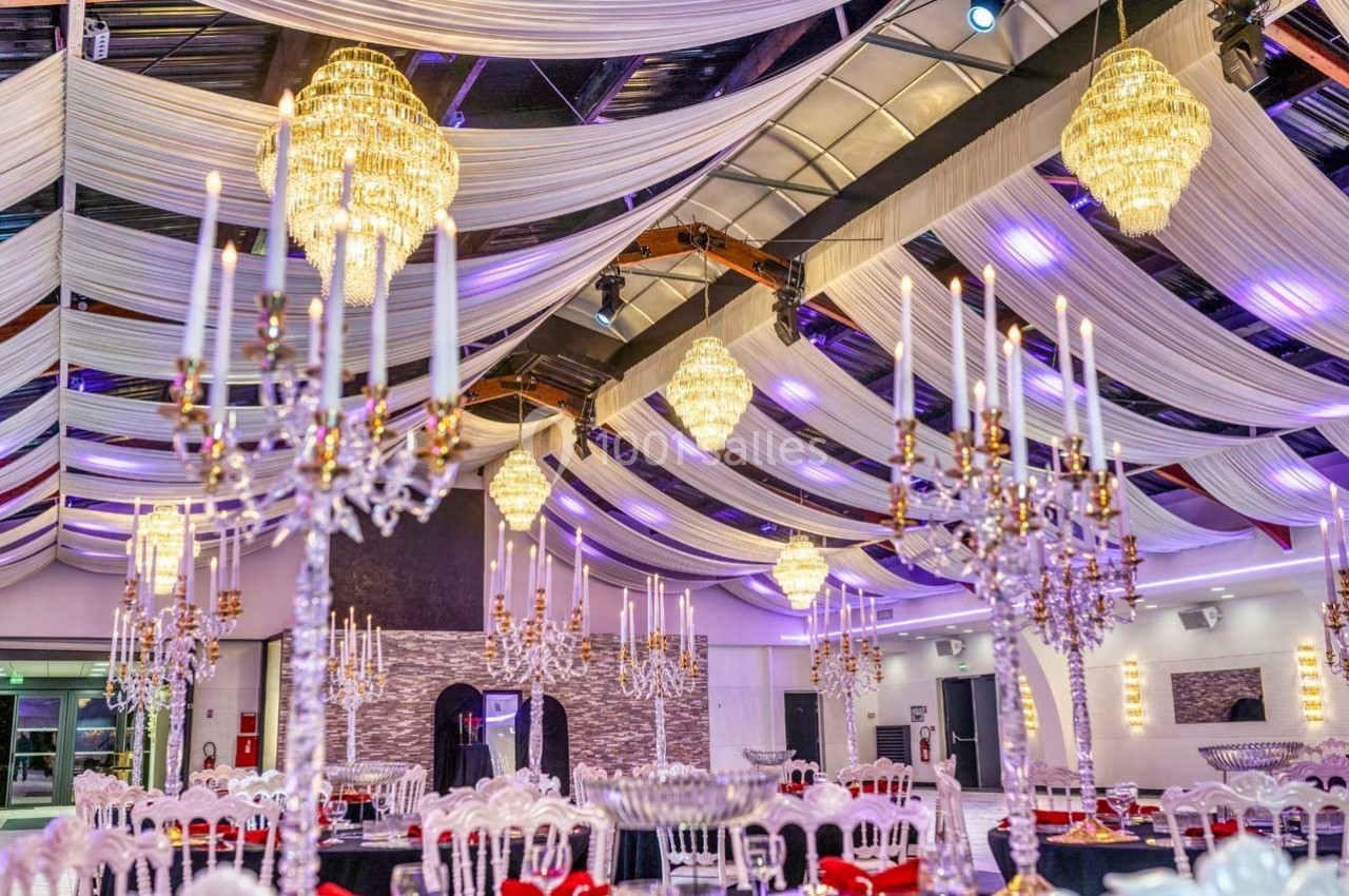 Salle de réception décorée avec des lustres, des chandeliers et des drapés suspendus sous un plafond voûté.
