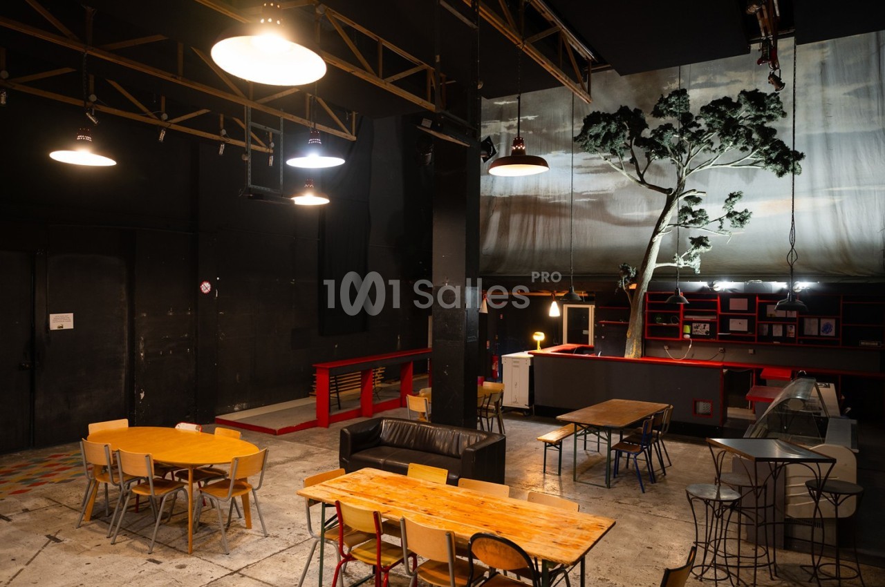 Salle intérieure avec tables, chaises, canapé et décor de scène comprenant un arbre artificiel et un éclairage tamisé.