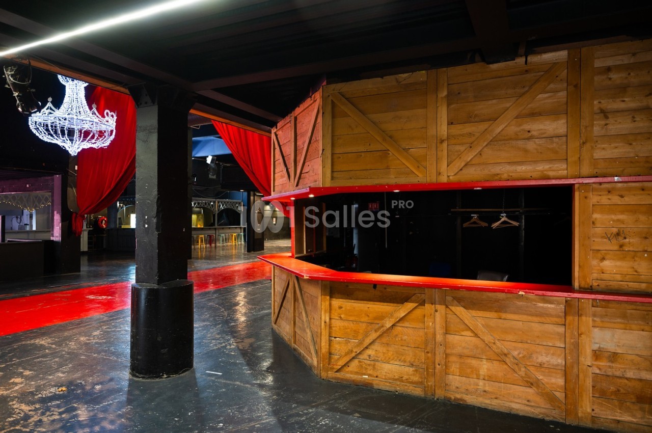 Intérieur d'une salle avec un comptoir en bois, des rideaux rouges et un lustre suspendu.