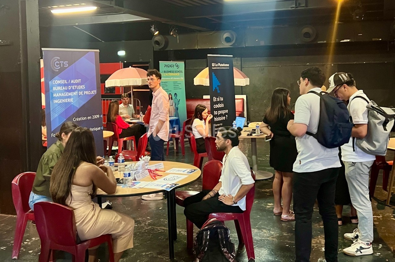 Des personnes échangent autour de stands d'information dans une salle avec des affiches et des tables.