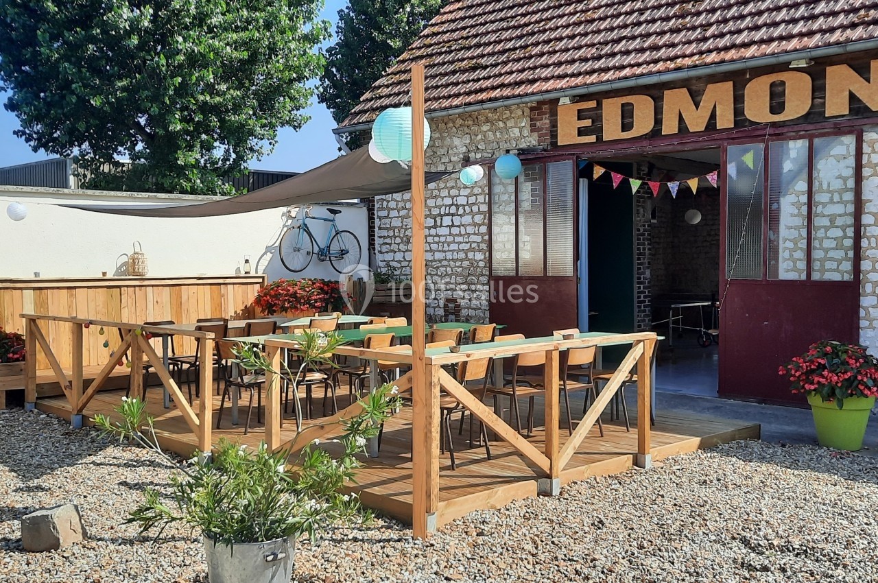 Terrasse en bois aménagée avec tables et chaises devant un bâtiment en briques portant l'inscription ’Edmond’.