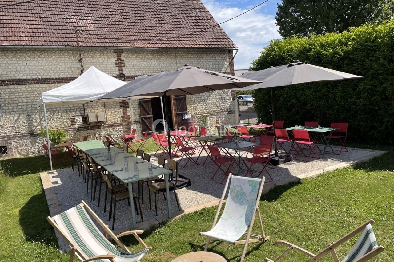 Terrasse aménagée avec tables, chaises et parasols devant une maison en pierre, entourée de verdure.