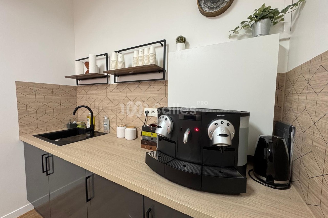 Cuisine moderne avec évier, machine à café automatique, bouilloire et étagères murales décorées.
