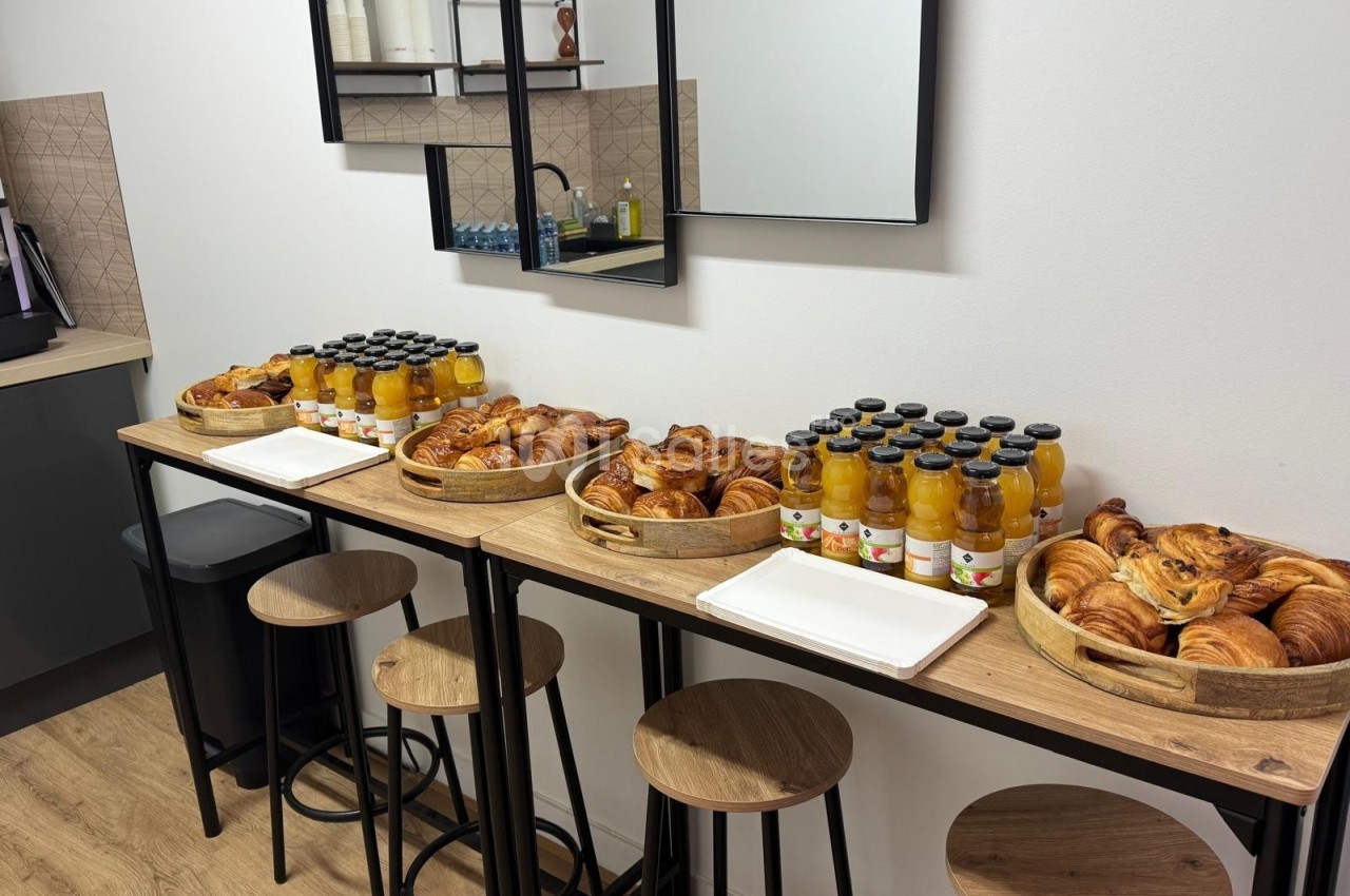 Plateau de viennoiseries et bouteilles de jus d'orange disposés sur une table haute dans une salle lumineuse.