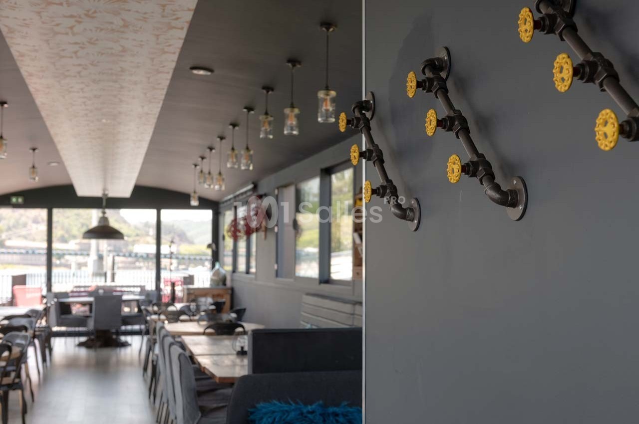 Intérieur d'un restaurant moderne avec des tables en bois, des luminaires suspendus et une décoration murale en tuyaux.
