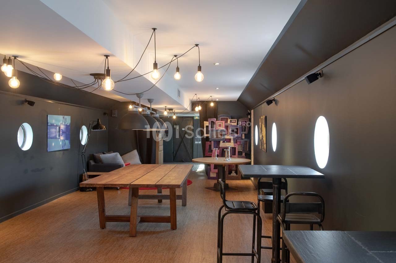 Salle moderne avec tables en bois, chaises noires, éclairage suspendu et décorations murales colorées.