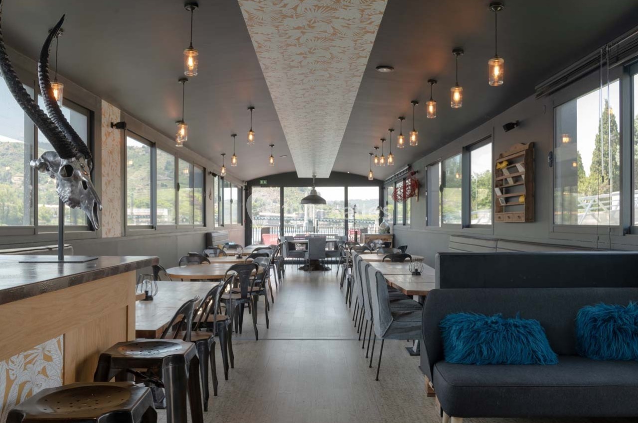 Salle de restaurant lumineuse avec tables en bois, chaises métalliques, banquettes et décoration moderne.