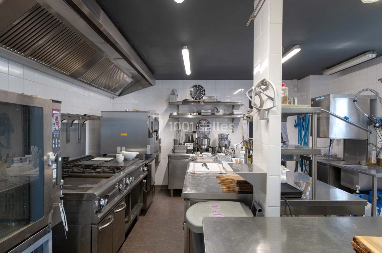 Cuisine professionnelle équipée avec des plans de travail en inox, appareils de cuisson et étagères de rangement.