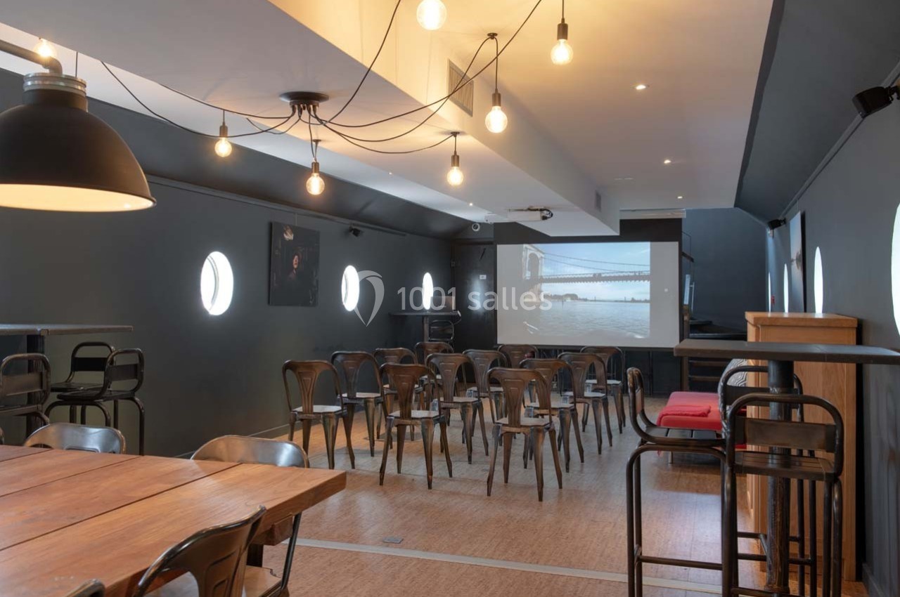 Salle de réunion avec chaises disposées face à un écran de projection, éclairée par des suspensions lumineuses.