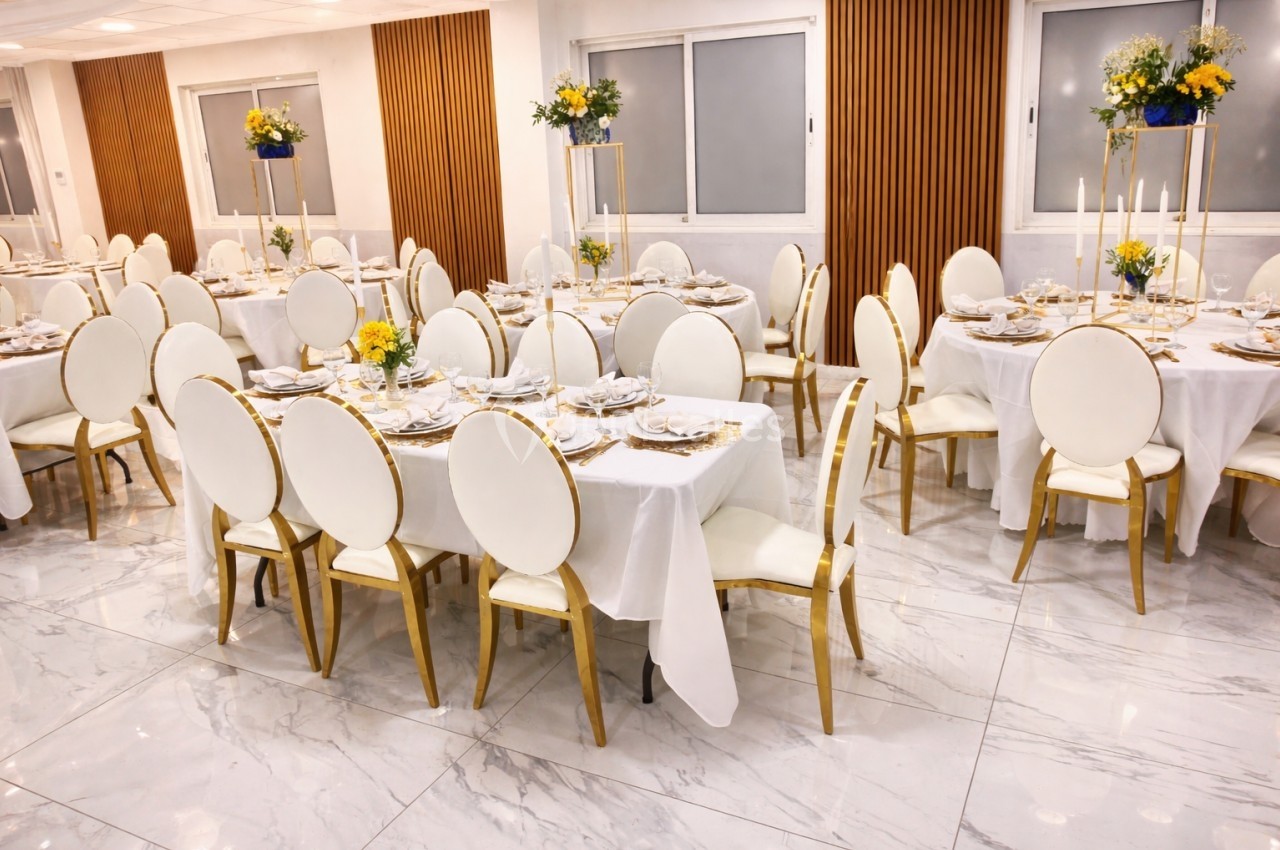 Salle de réception élégante avec tables dressées, chaises blanches et décorations florales jaunes et bleues.