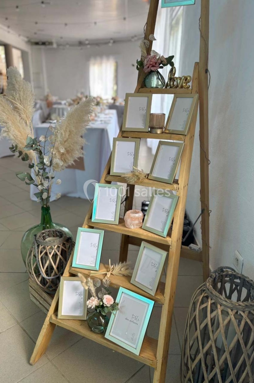 Échelle en bois décorée de cadres photo, fleurs et pampas, dans une salle de réception lumineuse.