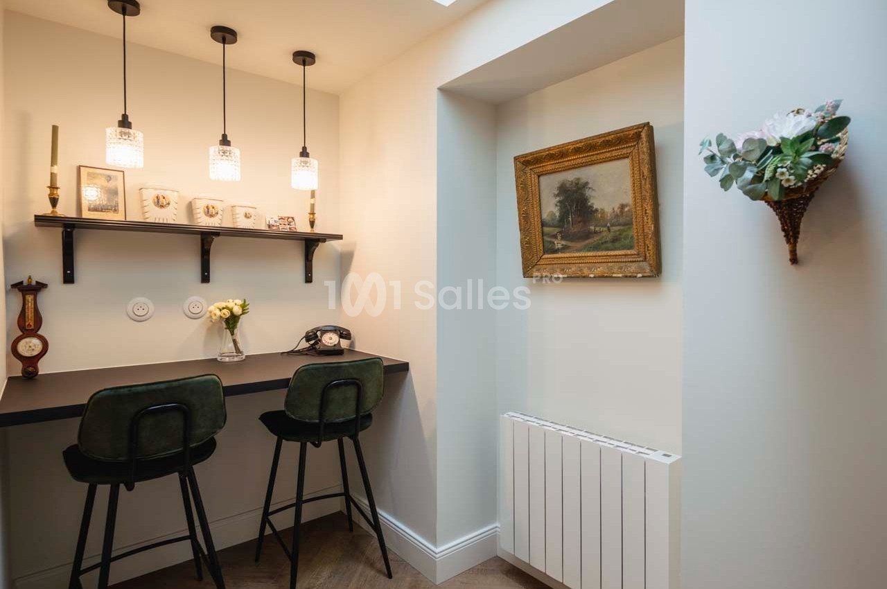 Coin bureau avec deux chaises hautes, étagère murale décorée, éclairage suspendu et tableau encadré sur le mur.