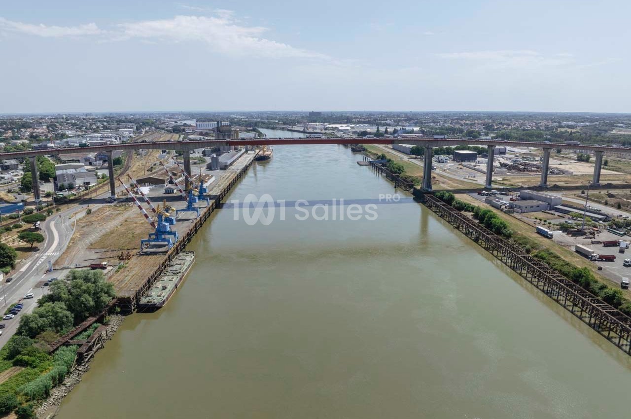 Vue aérienne d'un fleuve traversé par un pont, entouré de zones industrielles et d'infrastructures portuaires.